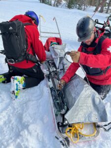 Person getting bundled up on a ski sled by ski patrollers
