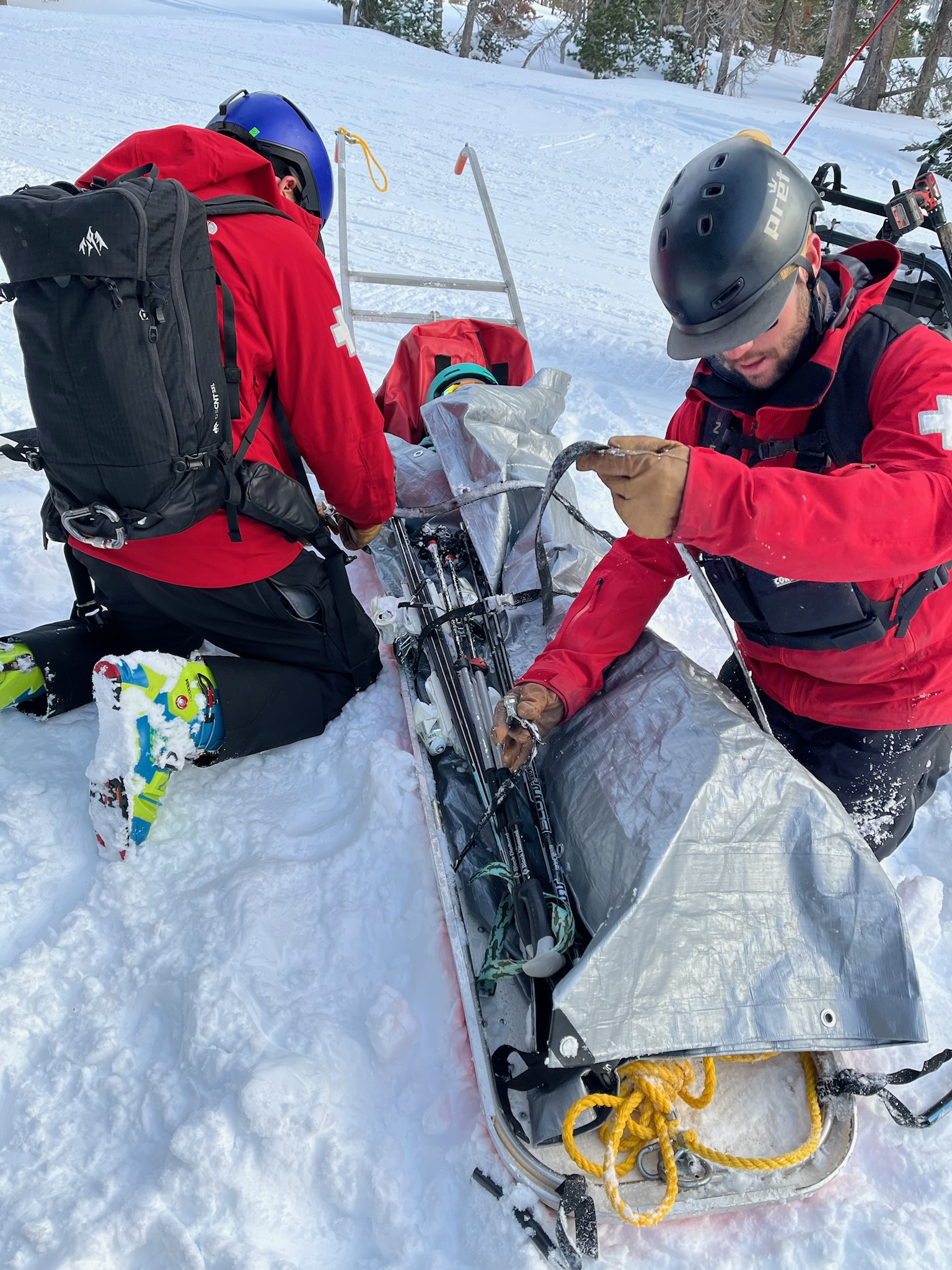Person getting bundled up on a ski sled by ski patrollers