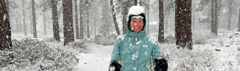 Smiling woman in the forest being covered with falling snow